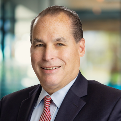 Chris Owens headshot, a smiling man with short dark hair, wearing a suit