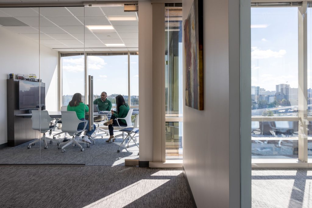 three people sitting in small office with glass divider and door