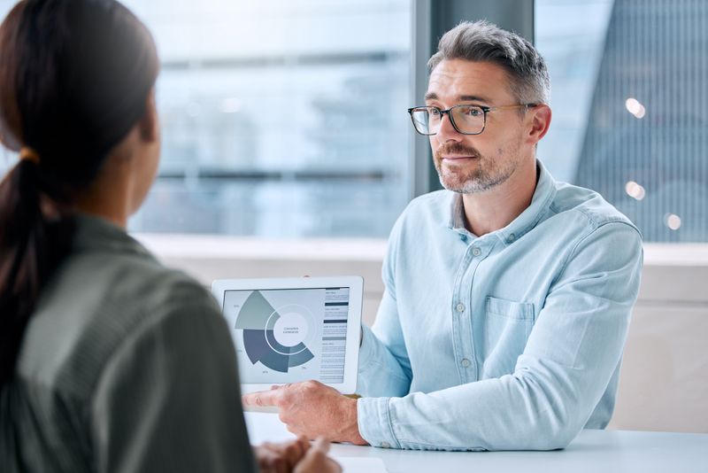 Man showing woman financial benefits and information on laptop.