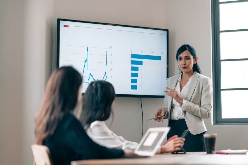 woman in blazer presenting to other women in meeting
