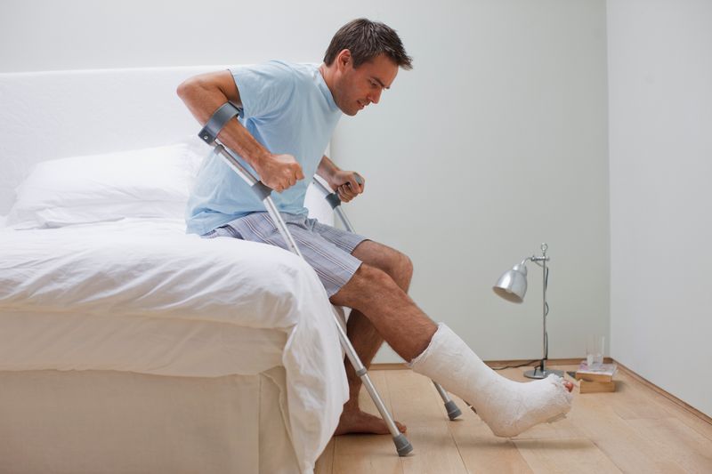 Man with a broken leg getting out of his bed with crutches