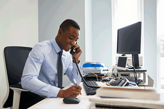 Smiling businessman sitting at desk and talking on office phone while holding dry erase marker