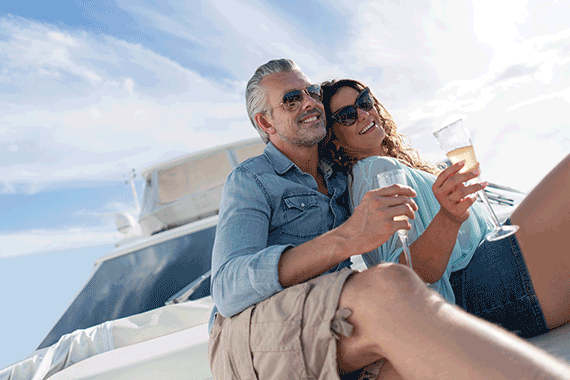 Couple in sunglasses smiling and cuddling on yacht with champagne flutes