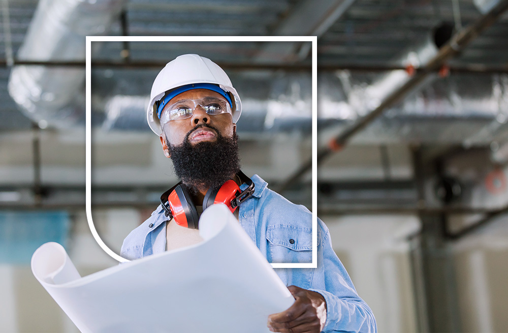 man wearing hardhat and safety glasses reviewing paper blueprints