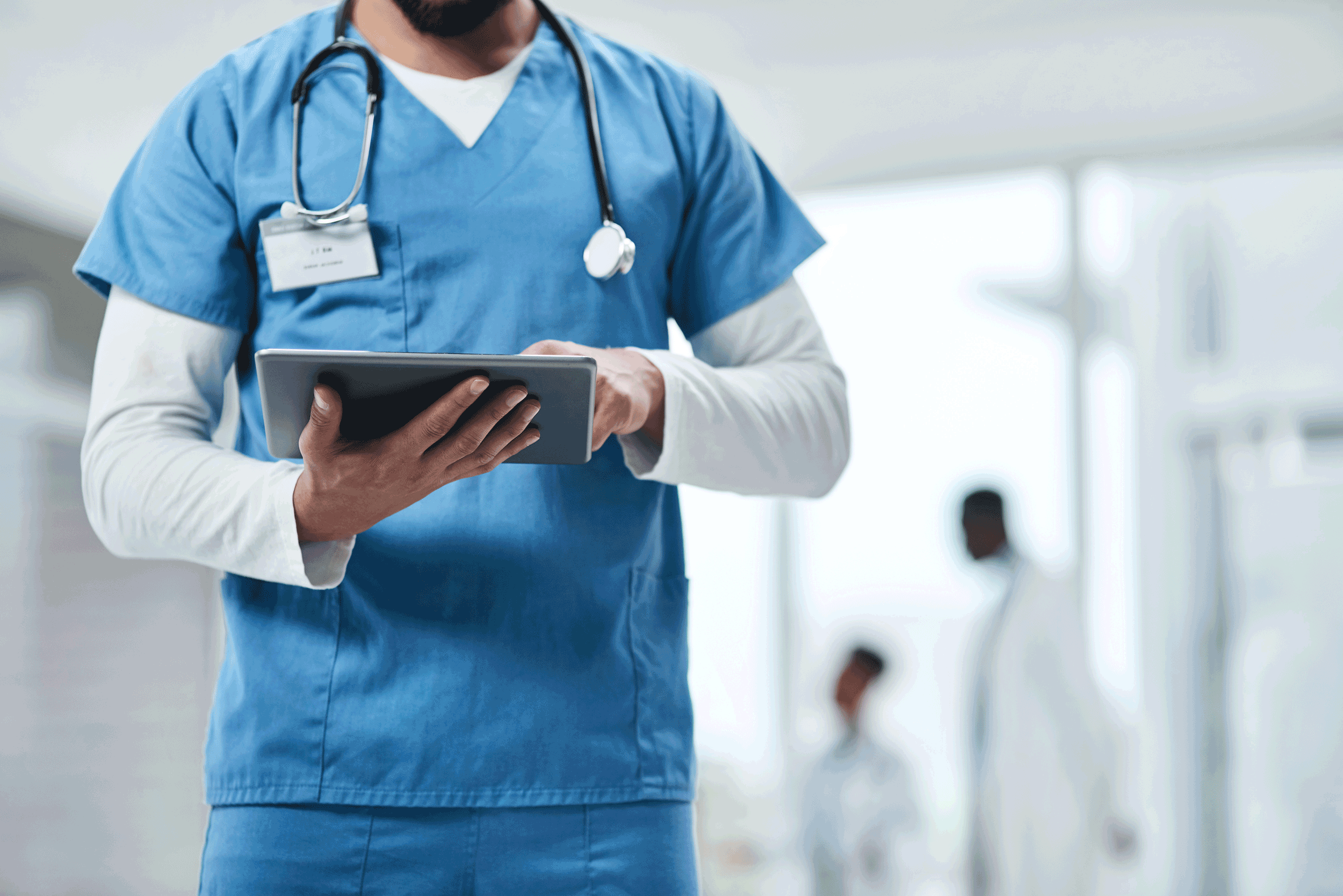 profile of medical professional in scrubs with stethoscope around their neck and holding a digital tablet
