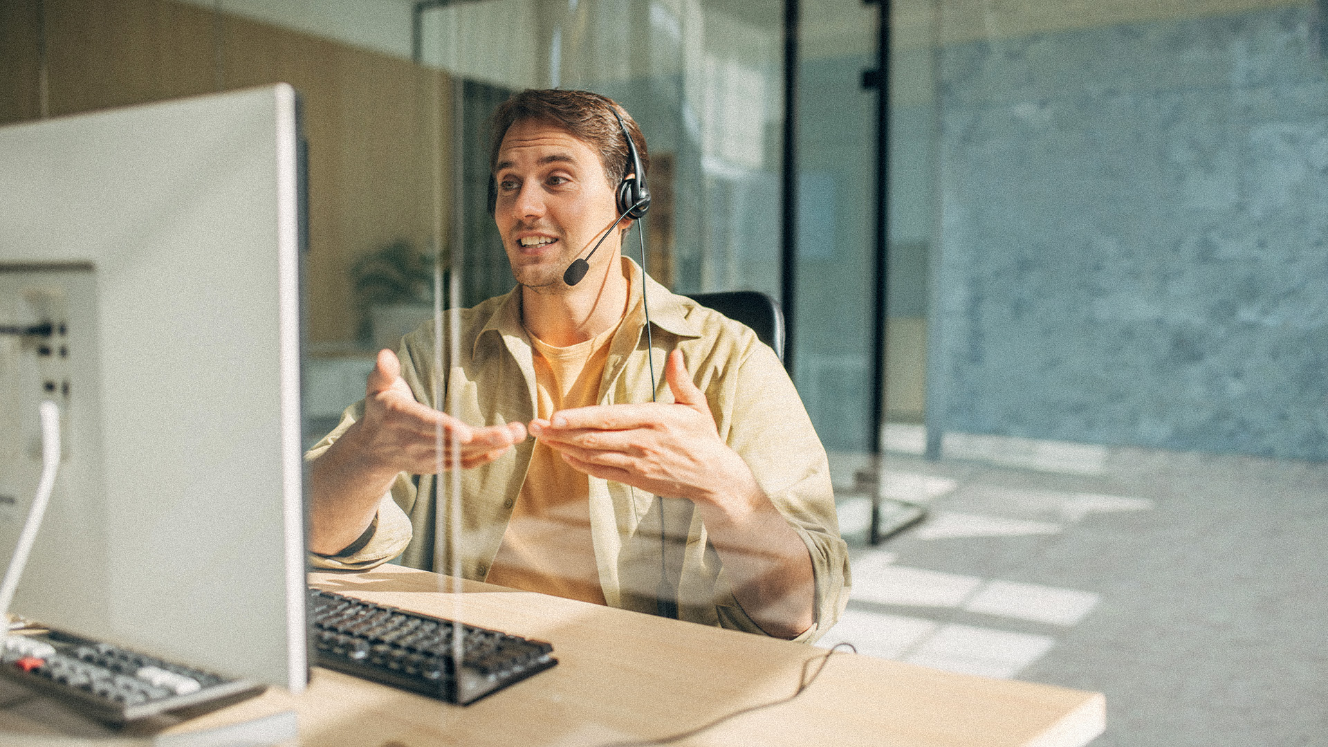person wearing headset talking and gesturing with hands in front of computer