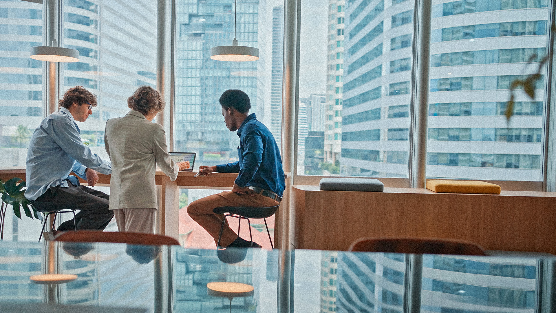 three professionals reviewing laptop in front of large windows with city view