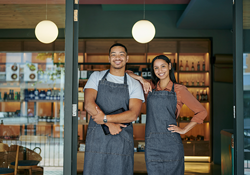 man and woman wearing denim aprons posing in front of small business front