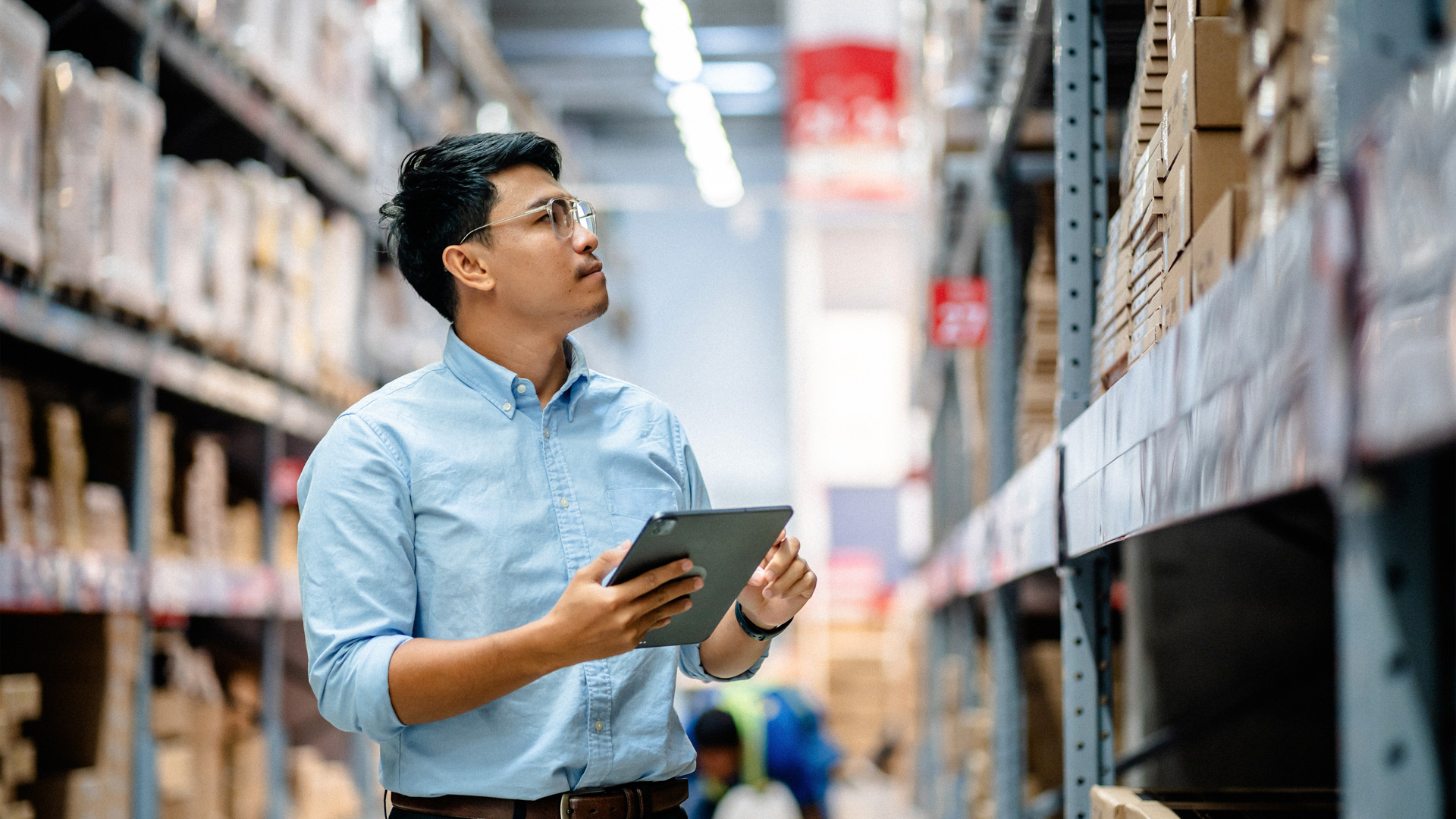 man wearing glasses and holding tablet reviewing contents on warehouse shelf